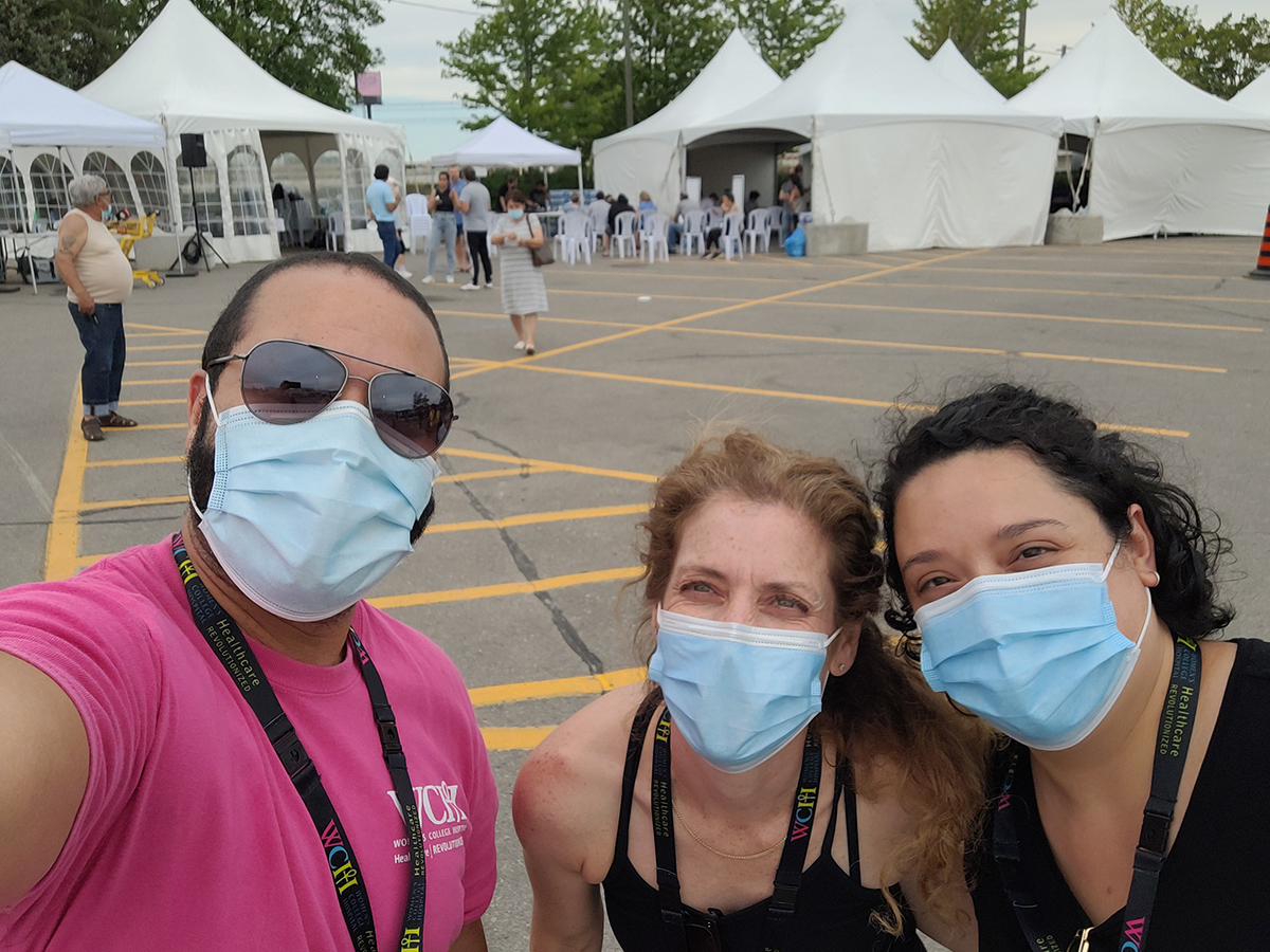 Three healthworkes wearing masks are in a parking lot with tents