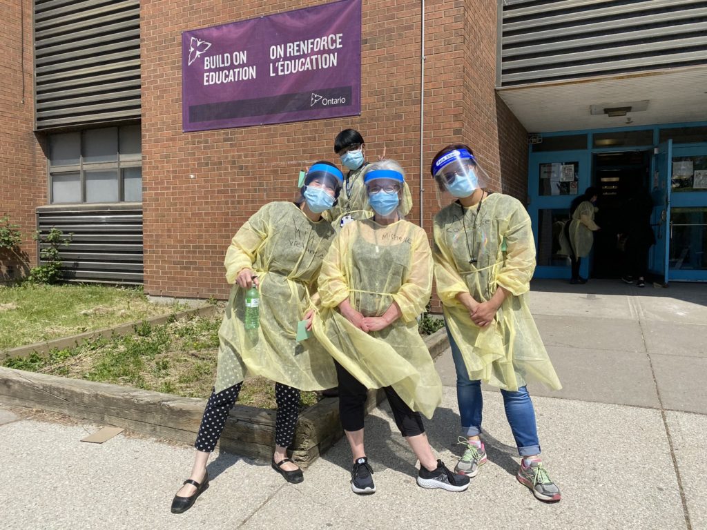 4 people in PPE pose in front of a school